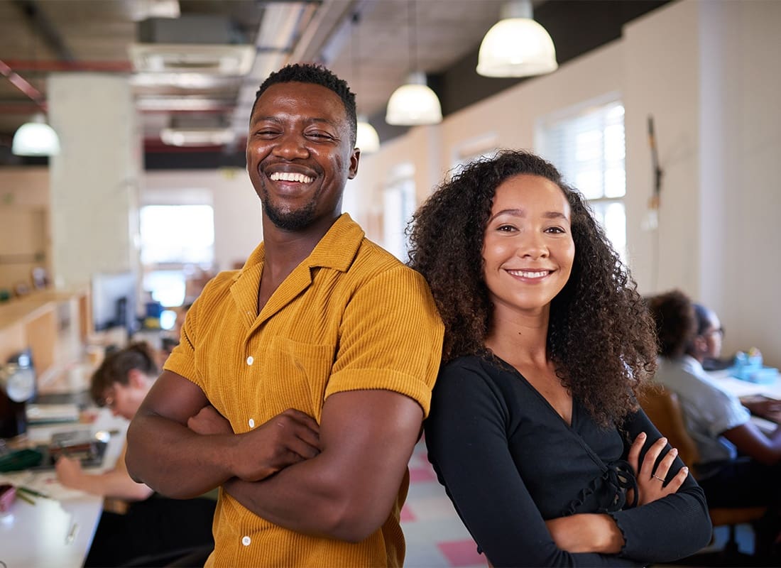 Business Insurance - Portrait of a Young Business Man and Woman Standing in Their Small Office with Their Arms Folded