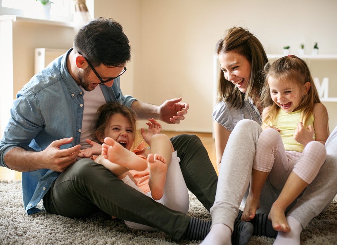 Personal Insurance - Cheerful Parents Having Fun Playing with Their Two Young Daughters at Home